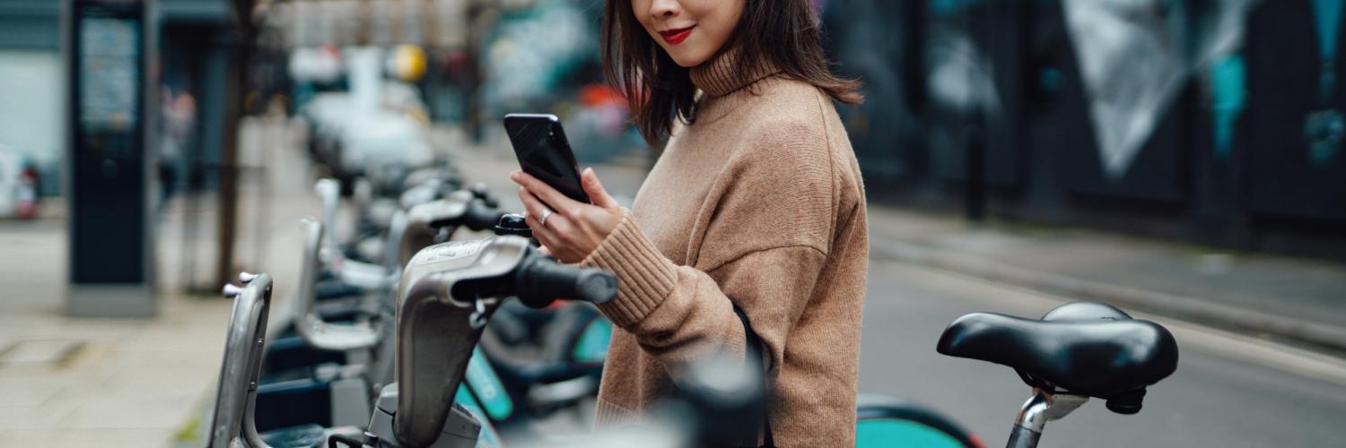 A woman next to electric bikes holding a mobile phone