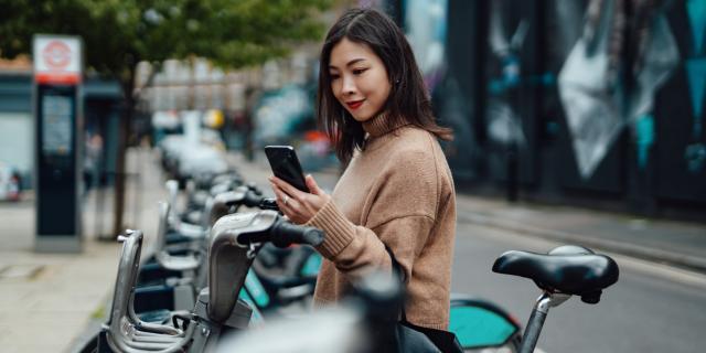 A woman next to electric bikes holding a mobile phone